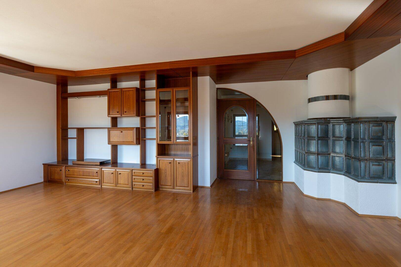 Geräumiges Wohnzimmer mit Holzboden und traditionellem Kachelofen, bereit zur individuellen Gestaltung.