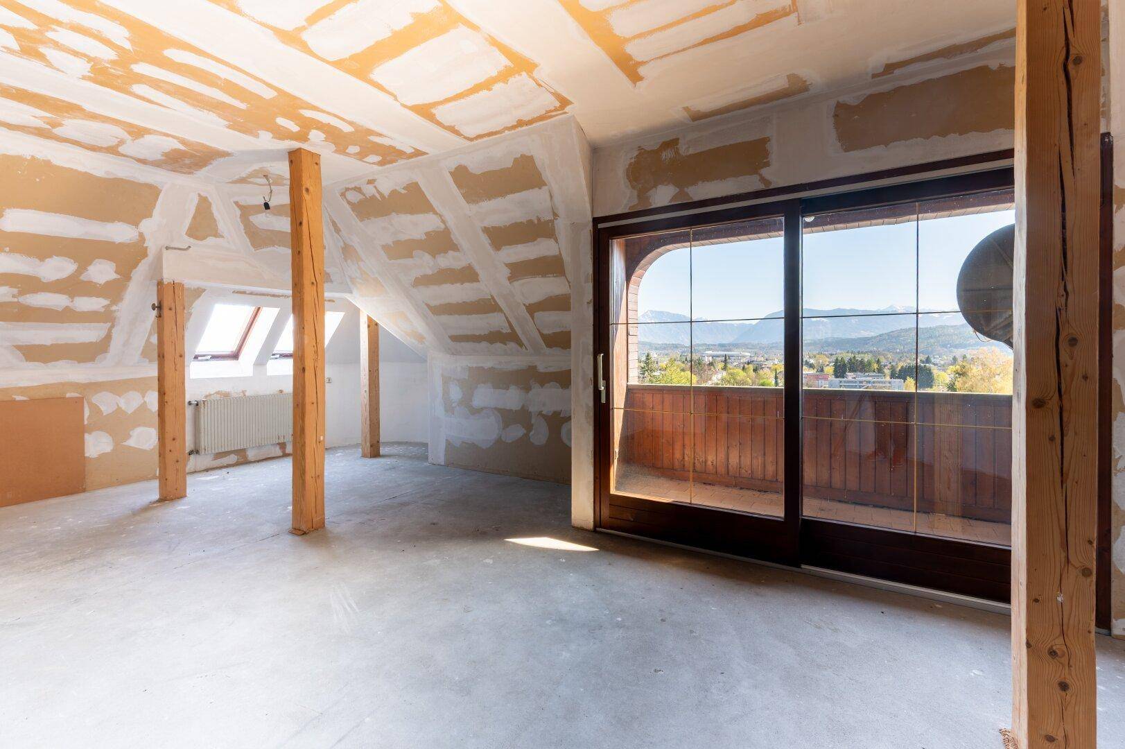 Ausbaufähiger Dachboden mit Holzbalken und großem Fenster, bietet Potenzial für zusätzlichen Wohnraum.