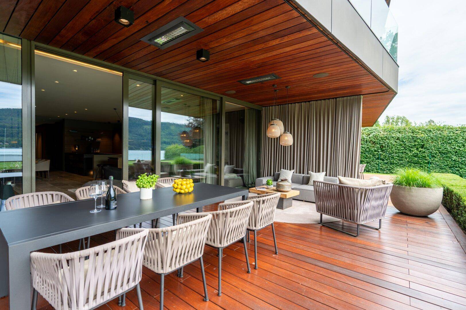 Überdachter Außenbereich mit großem Esstisch und gemütlicher Lounge, ideal für Mahlzeiten im Freien mit Seeblick.