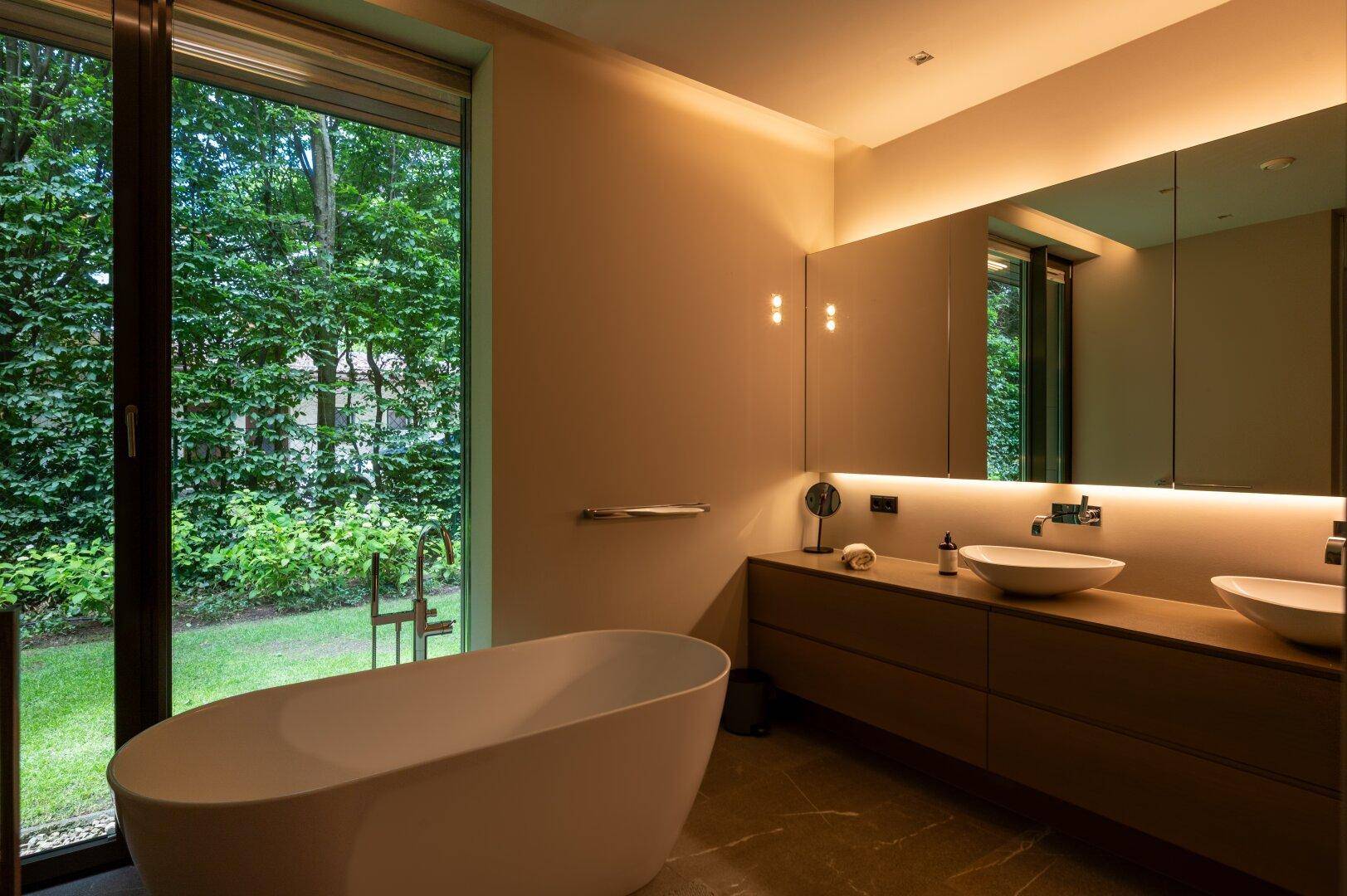 Modernes Badezimmer mit freistehender Badewanne, Doppelwaschbecken und großem Fenster mit Gartenblick.