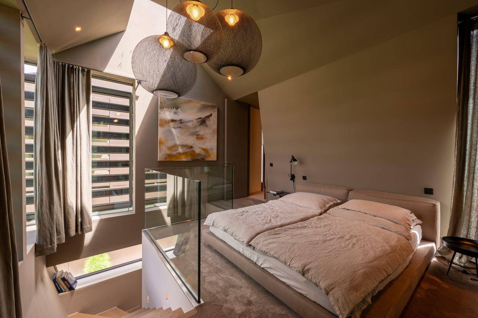 Helles Schlafzimmer mit großem Bett, modernen Leuchten und einer Treppe mit Glasgeländer.