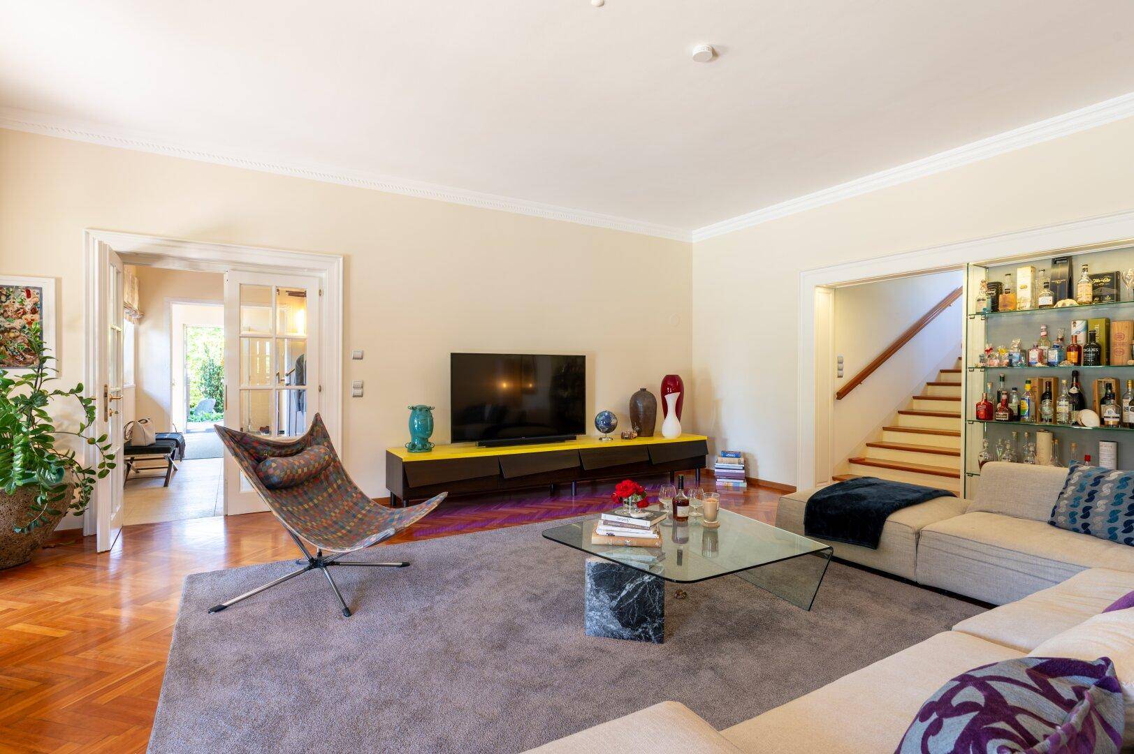 Helles Wohnzimmer mit Fischgrätparkett, großem Sofa und Zugang zu weiteren Räumen.