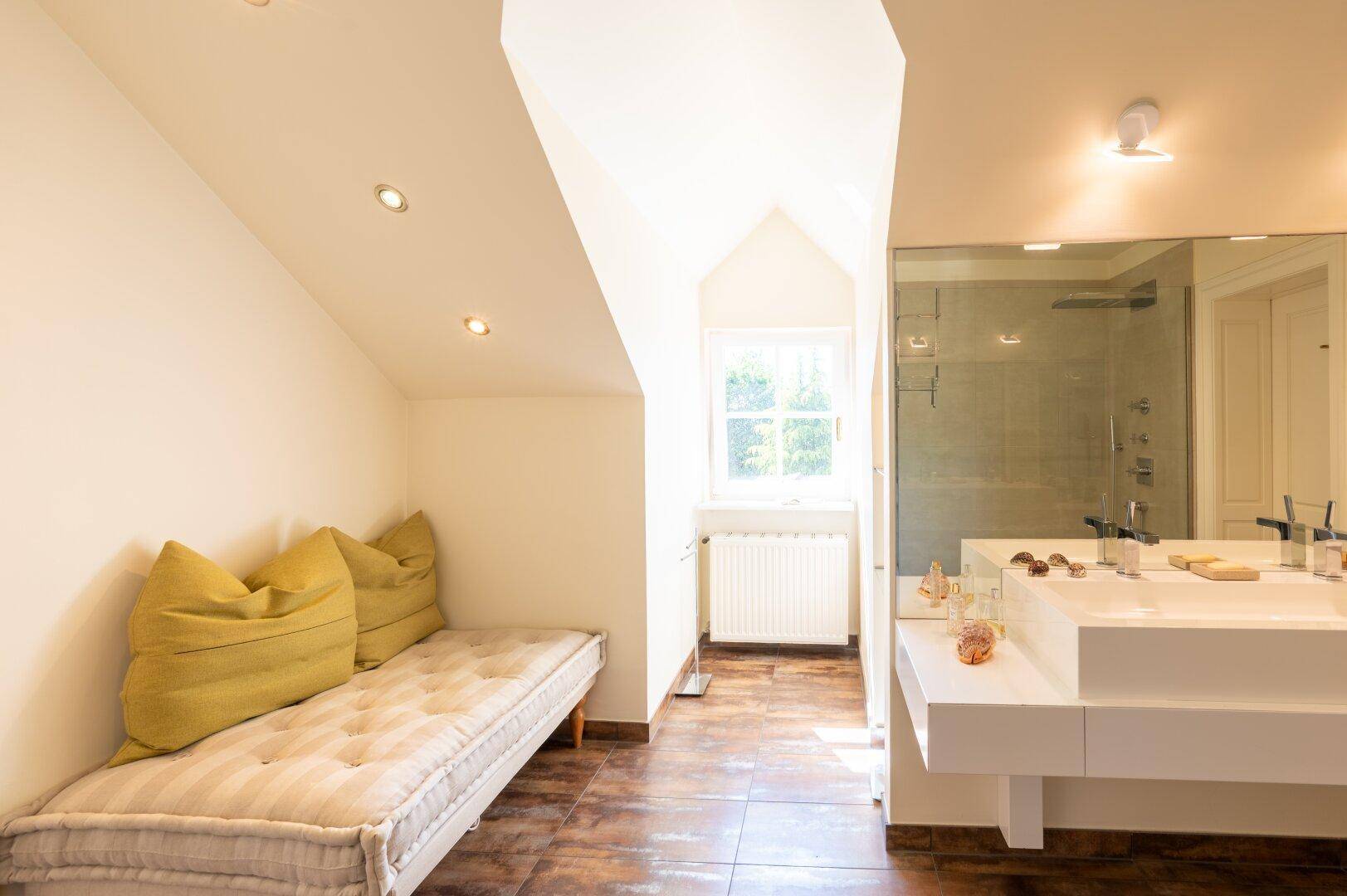 Geräumiges Badezimmer mit Doppelwaschbecken, Tagesbett und Dachschräge.