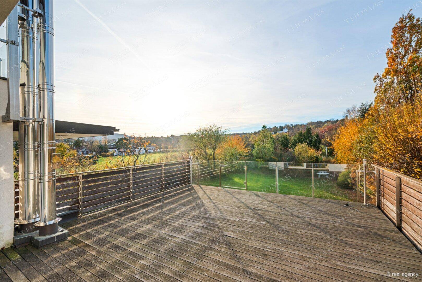 Geräumige Holzterrasse mit Glasgeländer und weitem Blick über die umliegende Landschaft.