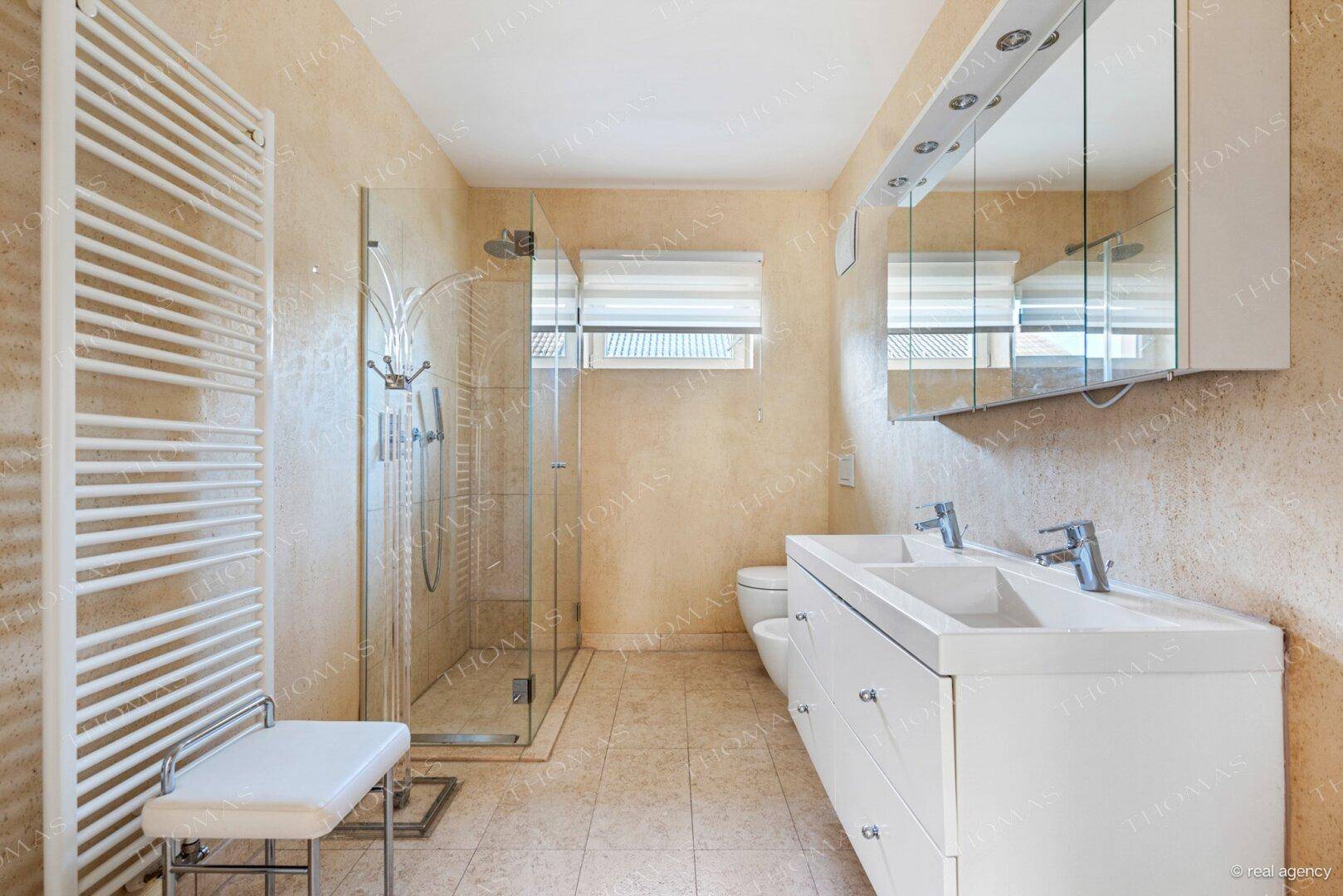 Helles Badezimmer mit großer Dusche, Doppelwaschbecken und beheiztem Handtuchhalter.
