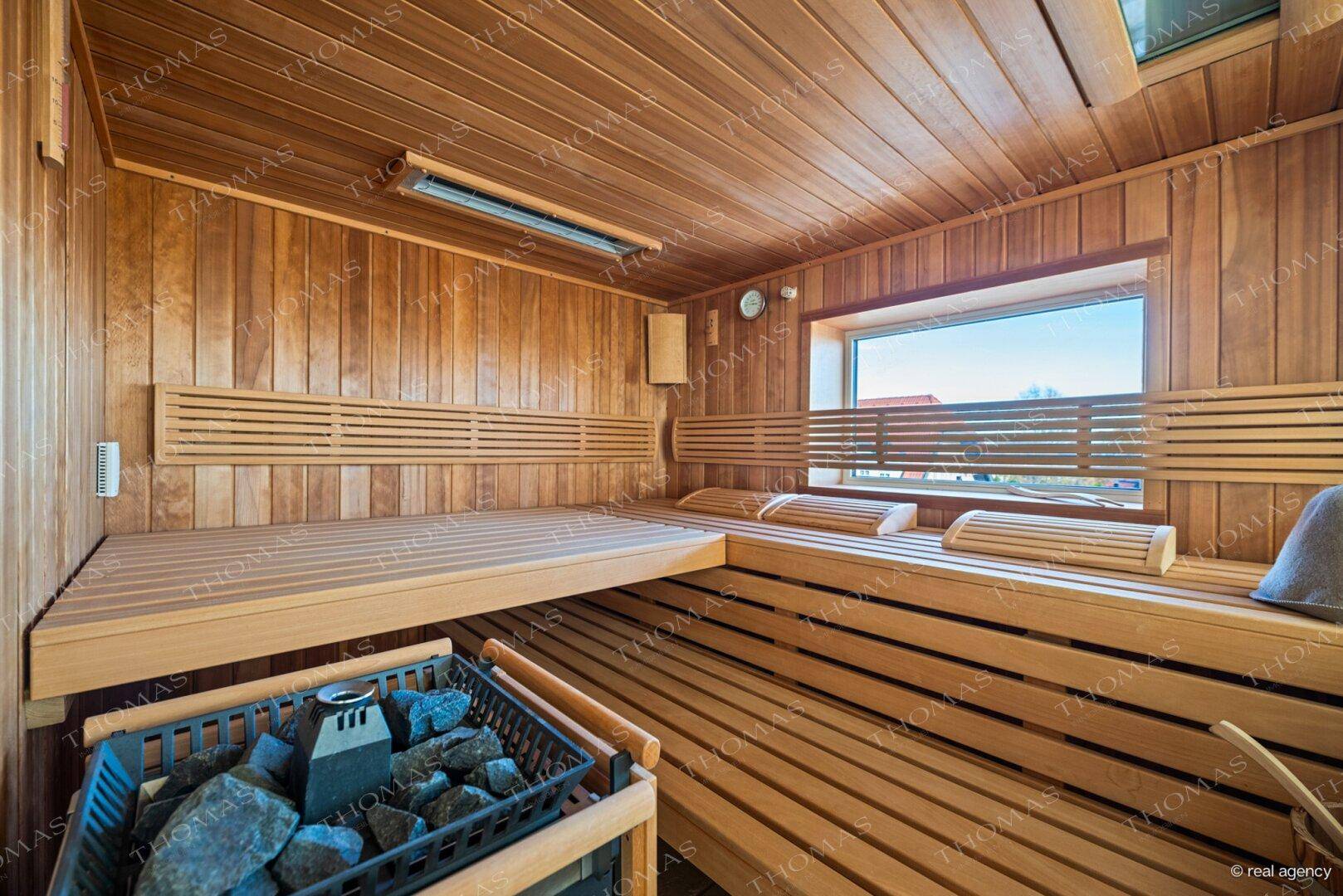 Geräumige Holzsauna mit mehreren Bänken und einem Fenster mit Blick ins Grüne.