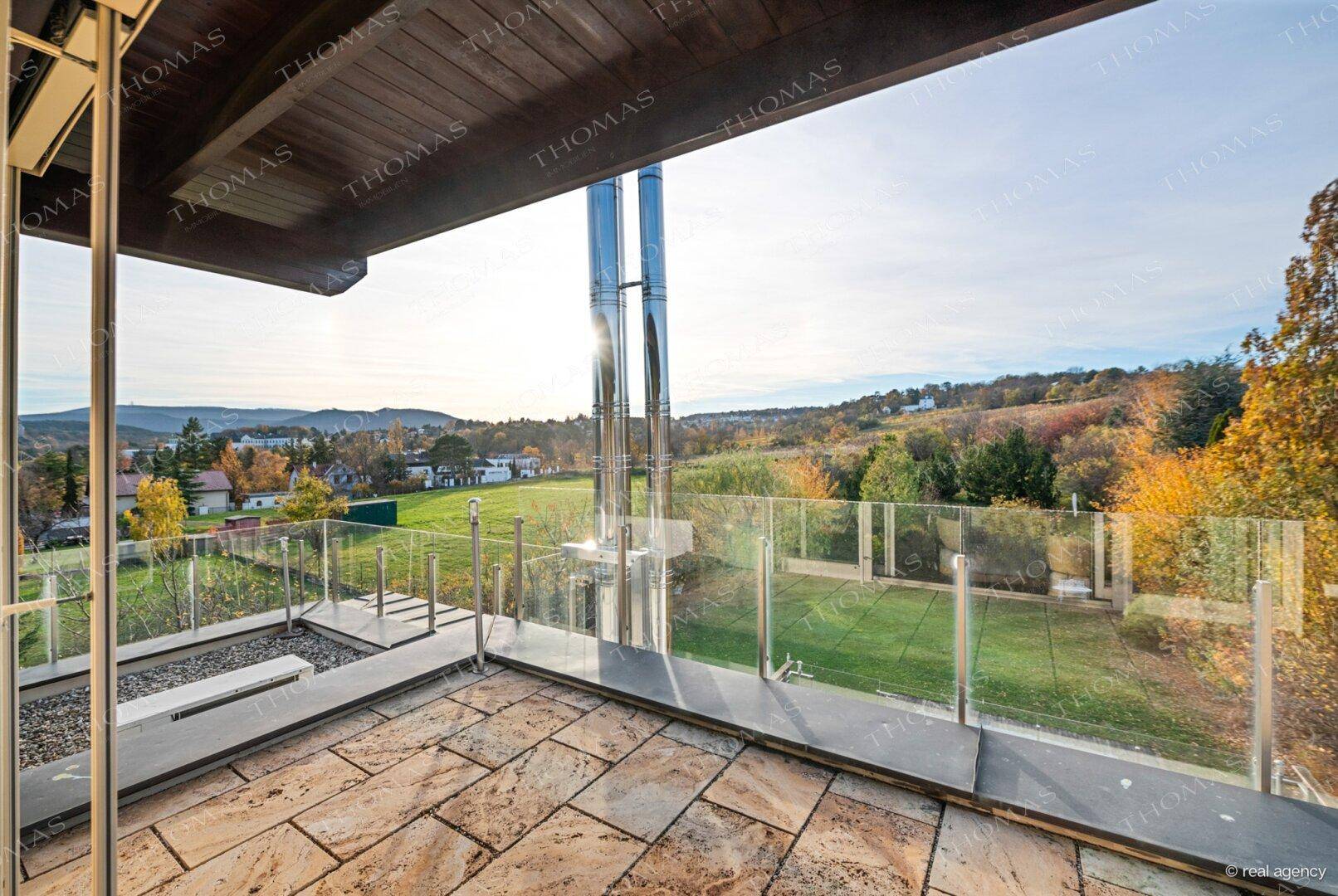 Sonniger Terrassenbereich mit Glasgeländer und weitem Blick über die herbstliche Landschaft.
