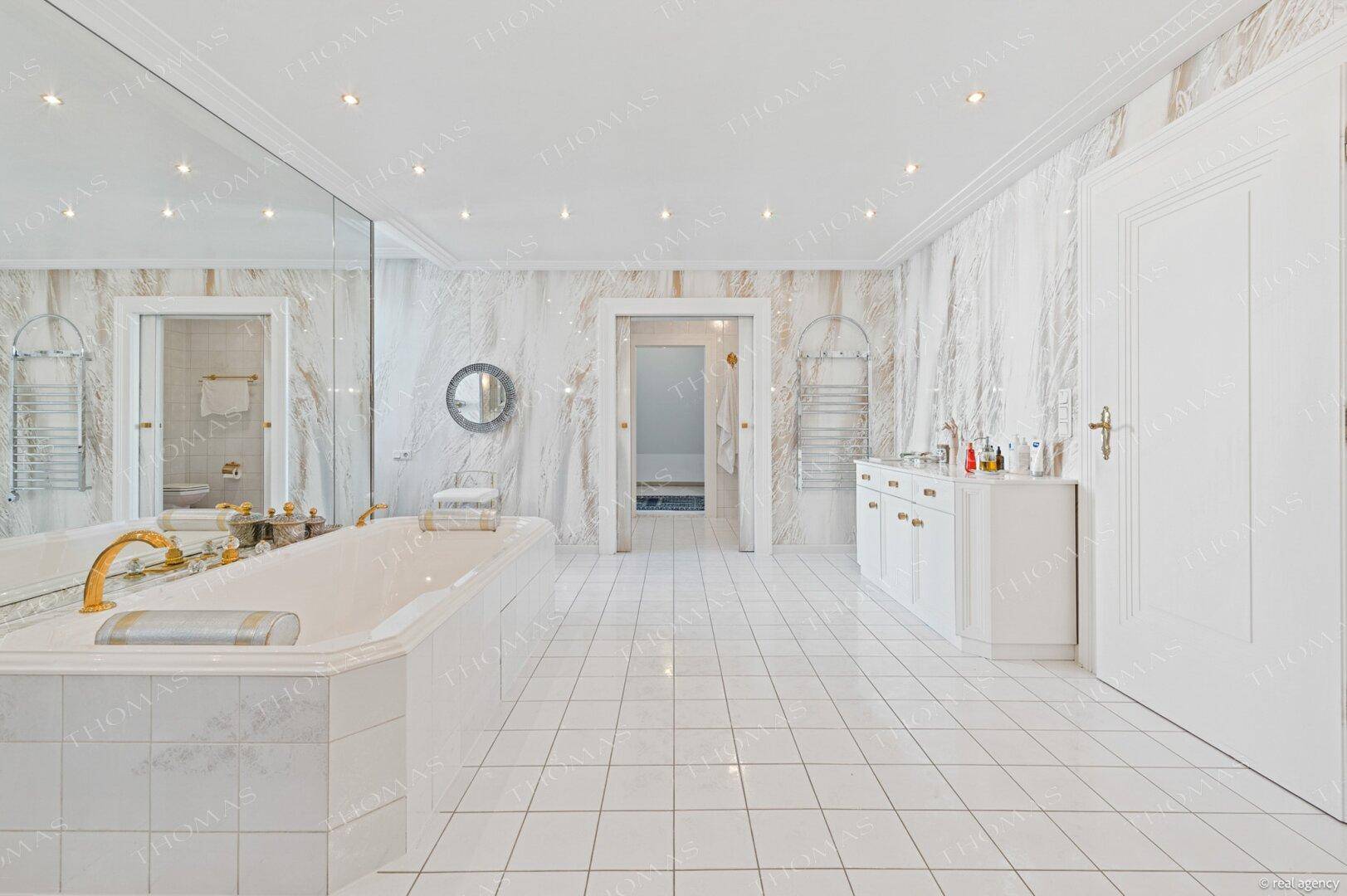 Luxuriöses Badezimmer mit Marmorwänden, großer Badewanne und Doppelwaschbecken.