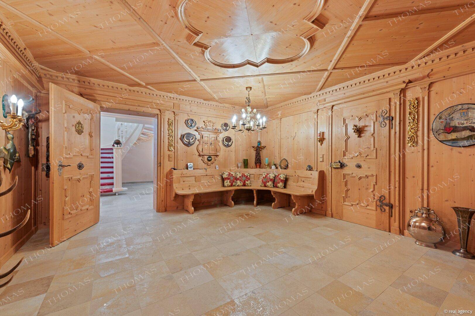 Rustikaler Raum mit aufwendiger Holzvertäfelung, Holzbänken und Kronleuchter.