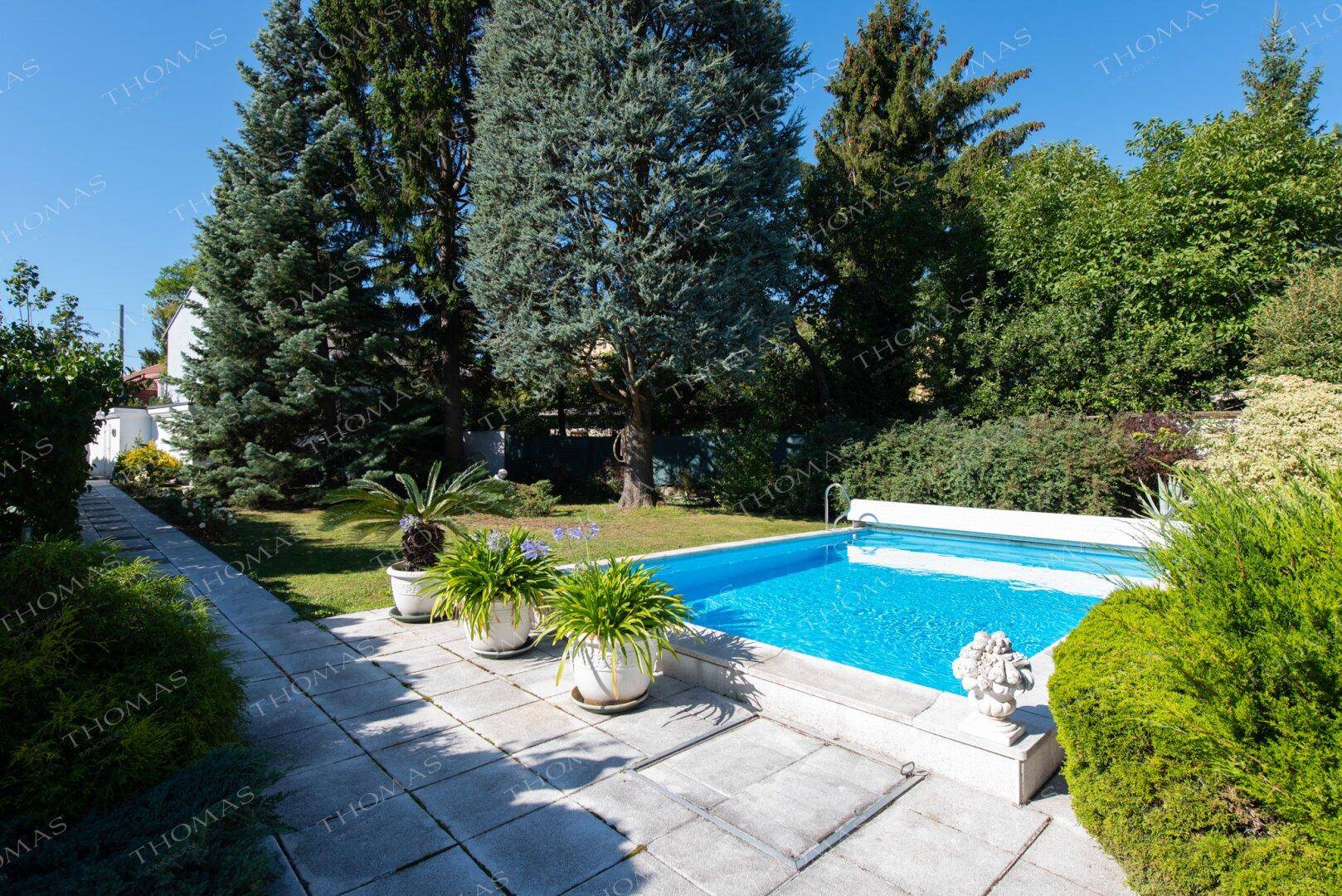 Gepflegter Gartenbereich mit Pool, großen Bäumen und sonnigen Liegeflächen.