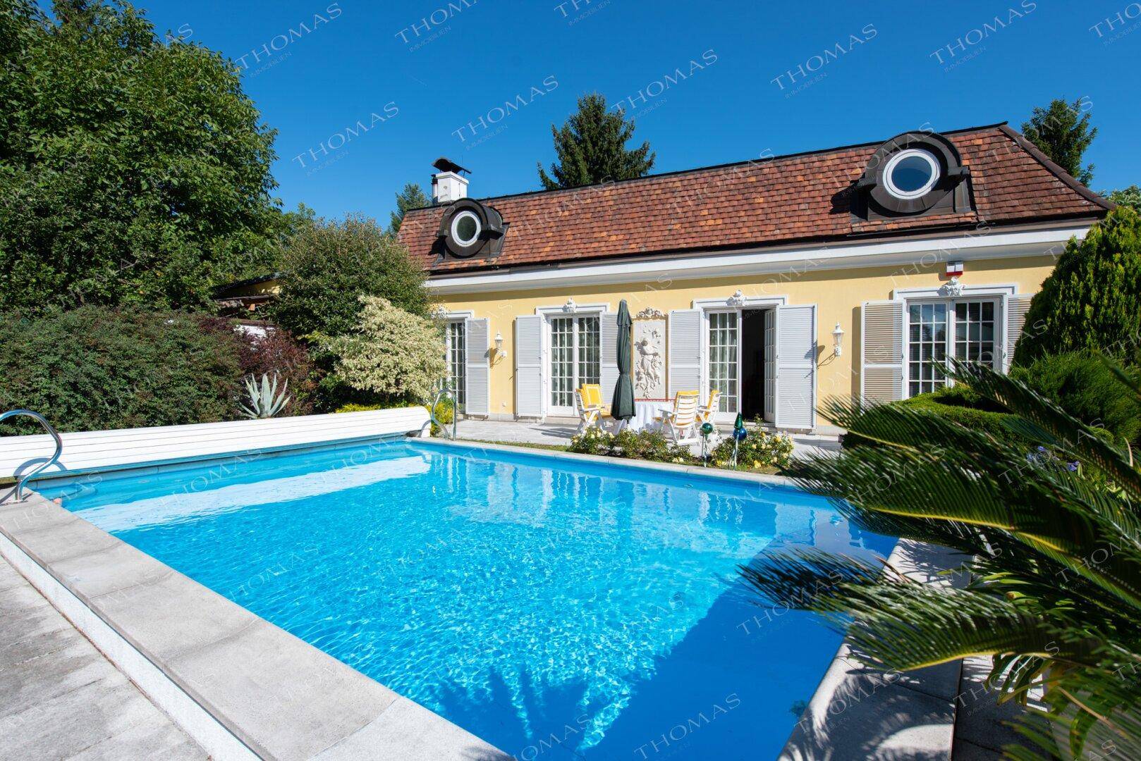 Großzügiger Außenbereich mit Schwimmbecken und Blick auf das charmante Wohnhaus.