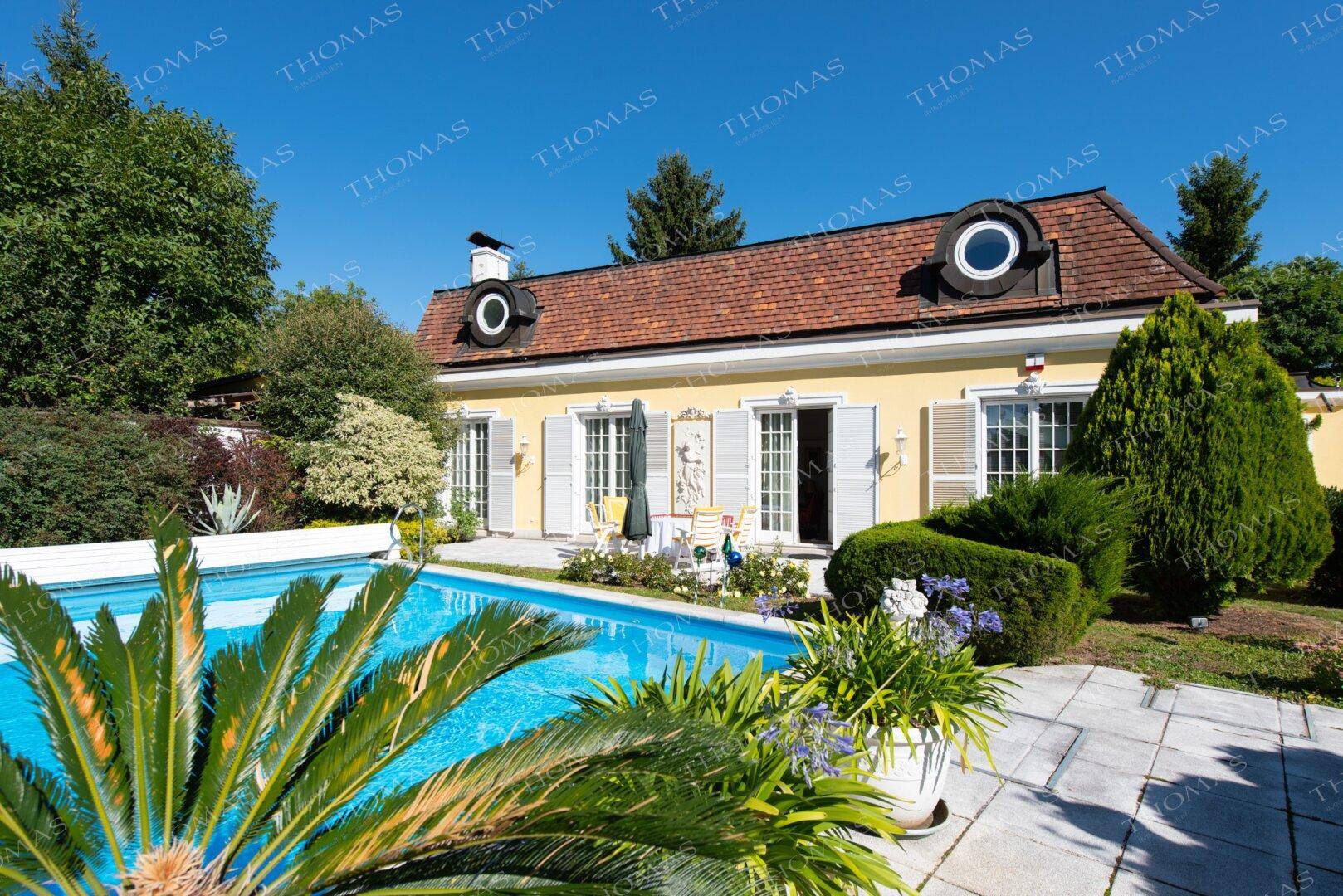 Charmantes Haus mit großem Außenpool und gepflegtem Garten unter blauem Himmel.