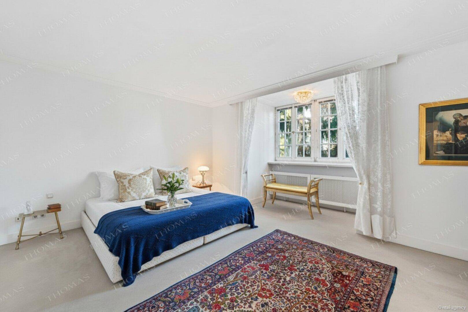 Helles Schlafzimmer mit Teppichboden, großem Bett und Blick in den grünen Garten.
