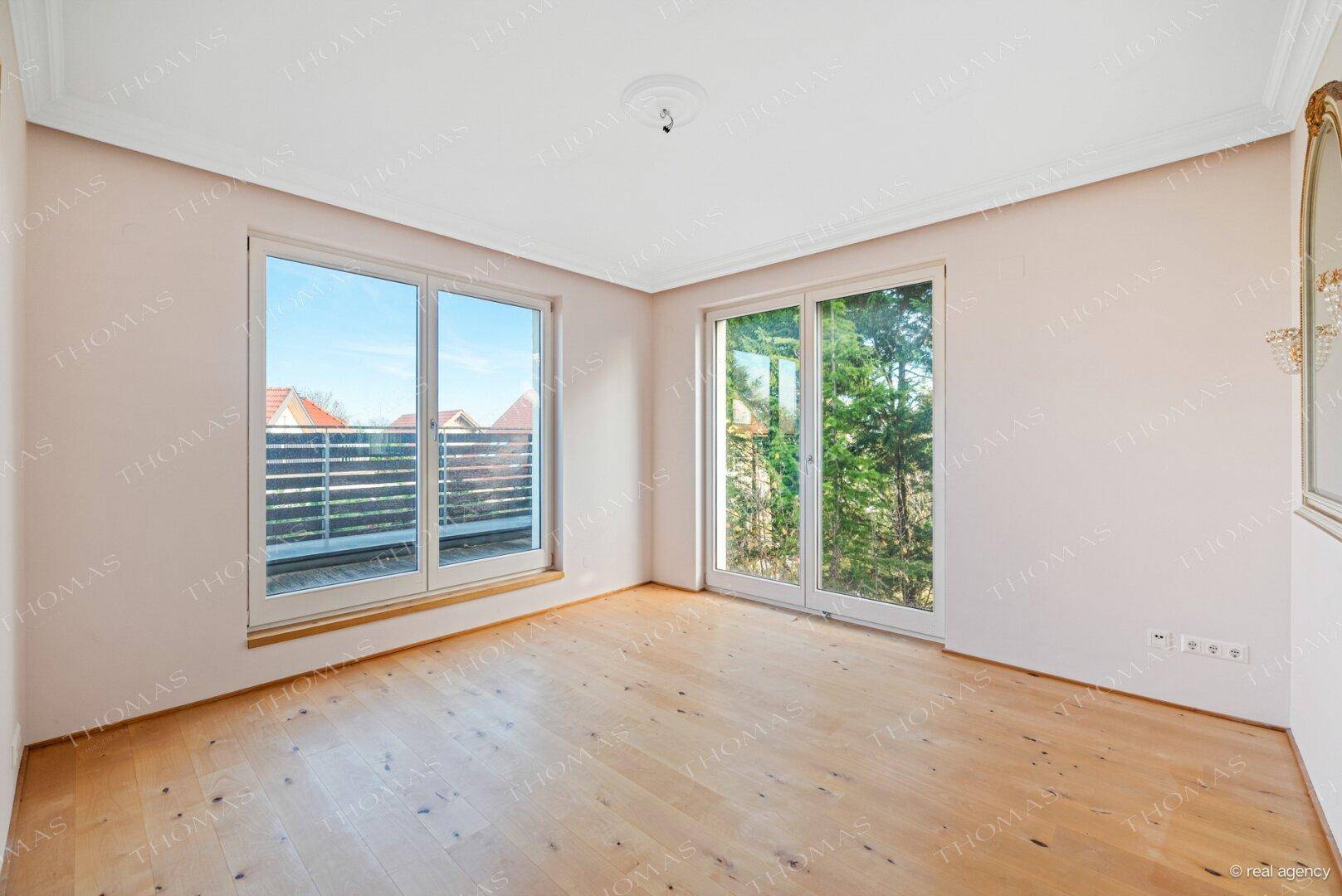 Helles Zimmer mit Holzboden und Zugang zu einem Balkon mit weitem Ausblick.