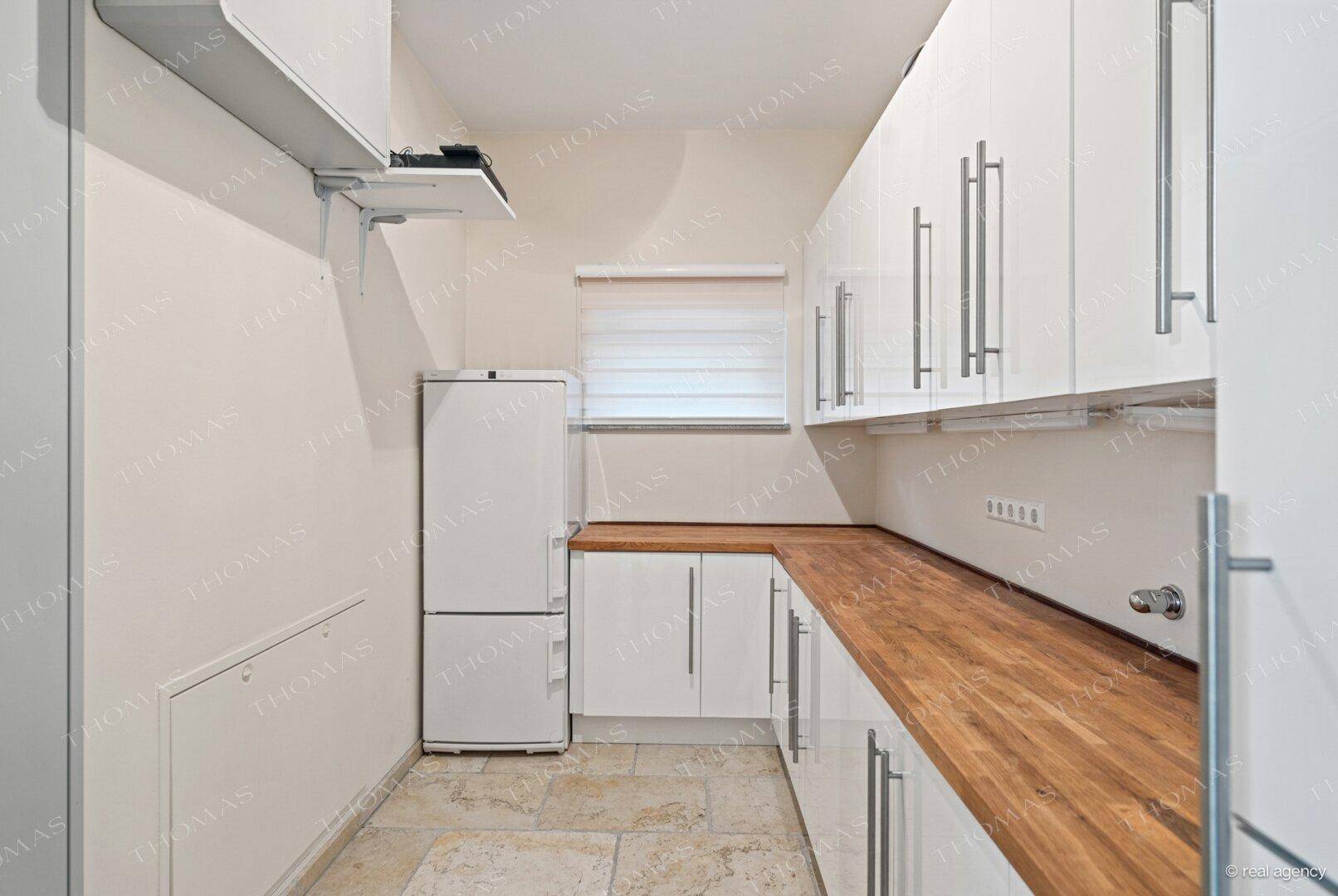 Praktische Nebenküche mit weißen Schränken, Holz-Arbeitsplatte und Fliesenboden.