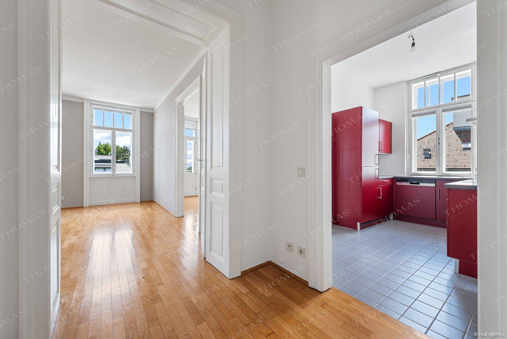 Flur mit Parkettboden und Blick in eine moderne Küche mit roten Schränken und Fenster.