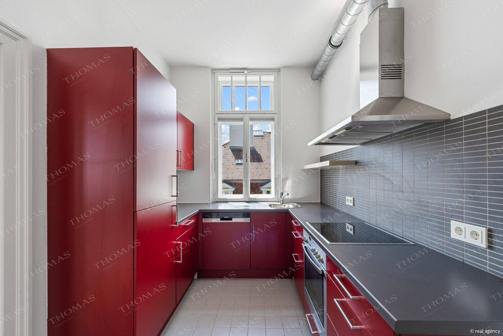 Moderne Küche mit leuchtend roten Schränken, Induktionskochfeld und praktischer Dunstabzugshaube.