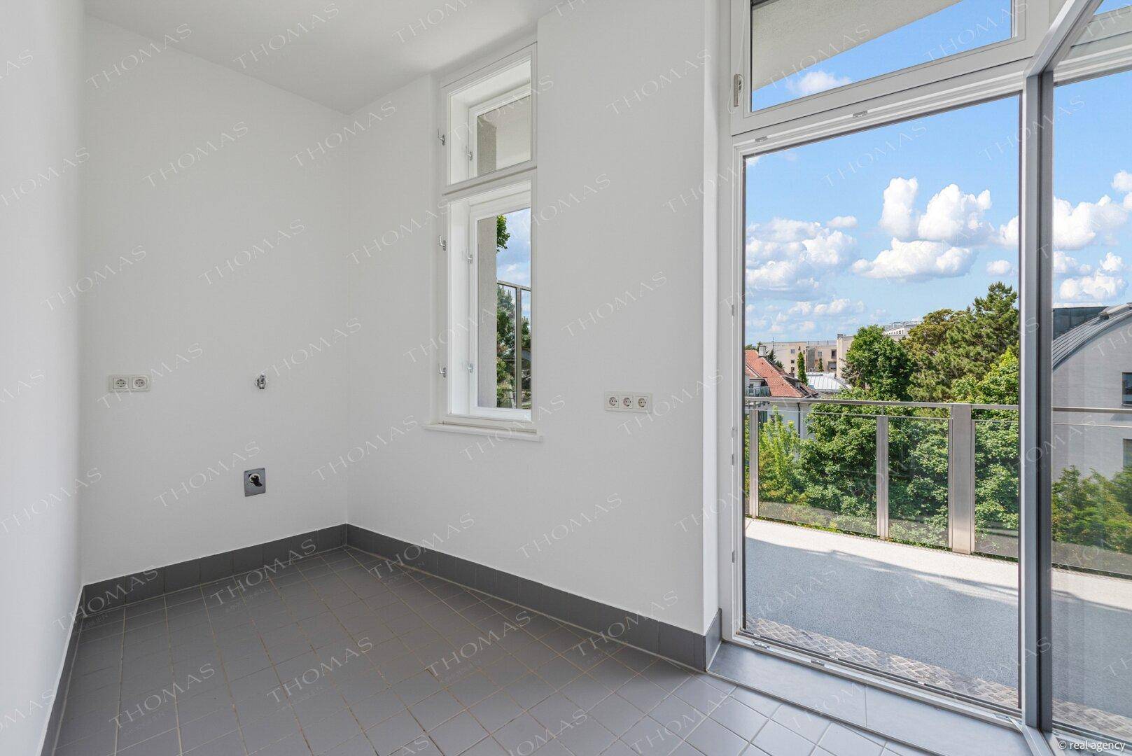 Heller Hauswirtschaftsraum mit Fliesenboden und großem Fenster, mit Zugang zum Balkon.