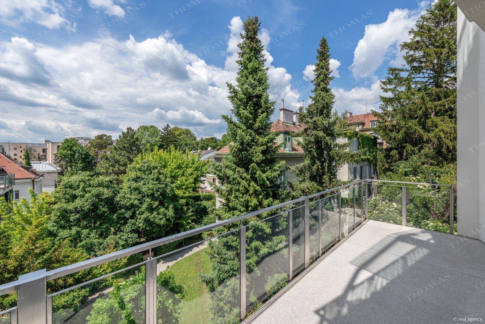 Sonniger Balkon mit modernem Glasgeländer und einem schönen Ausblick auf die umliegende Natur.