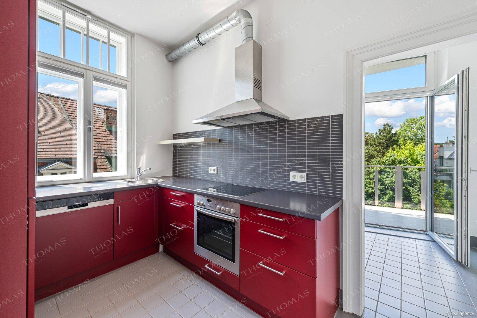 Funktionale Küche mit roten Fronten, modernen Geräten und direktem Zugang zu einem Balkon.