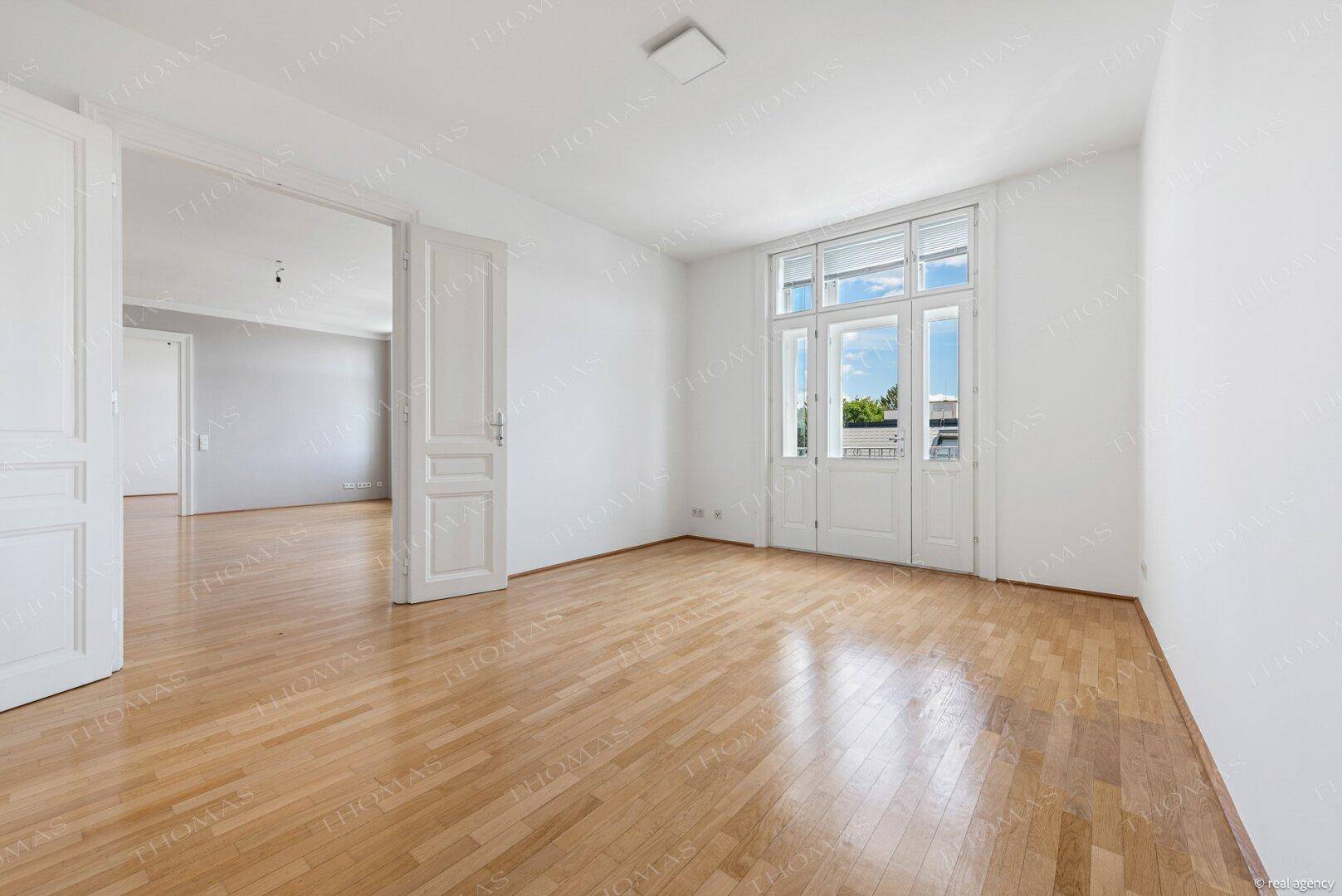Heller Raum mit Holzboden und großen Fenstertüren, die viel Tageslicht hereinlassen.