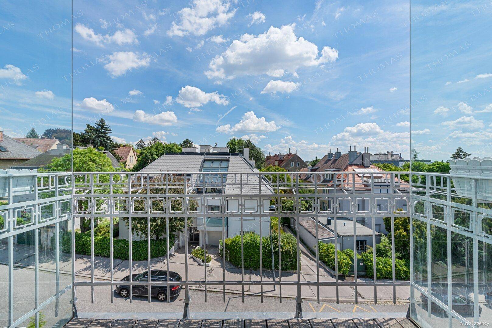 Balkon mit Metallgeländer und Blick auf eine ruhige Wohnstraße mit gepflegten Häusern.