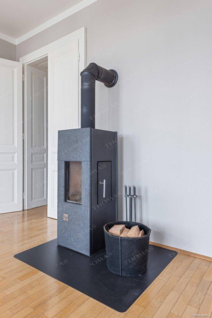Moderner Kaminofen mit Holzscheiten auf glänzendem Parkettboden, bereit für gemütliche Abende.