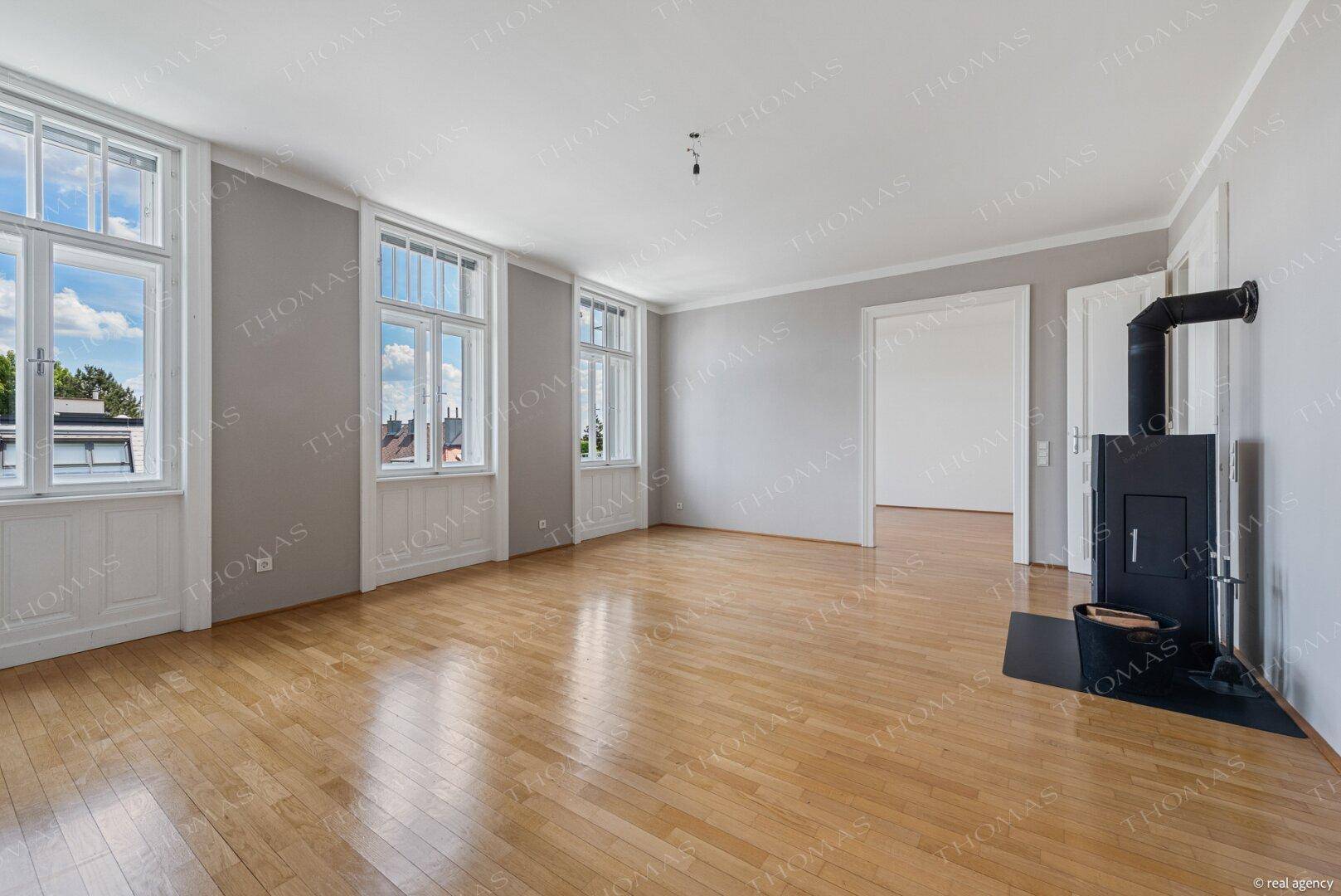Lichtdurchflutetes Wohnzimmer mit elegantem Parkett und einem modernen Kaminofen als Blickfang.