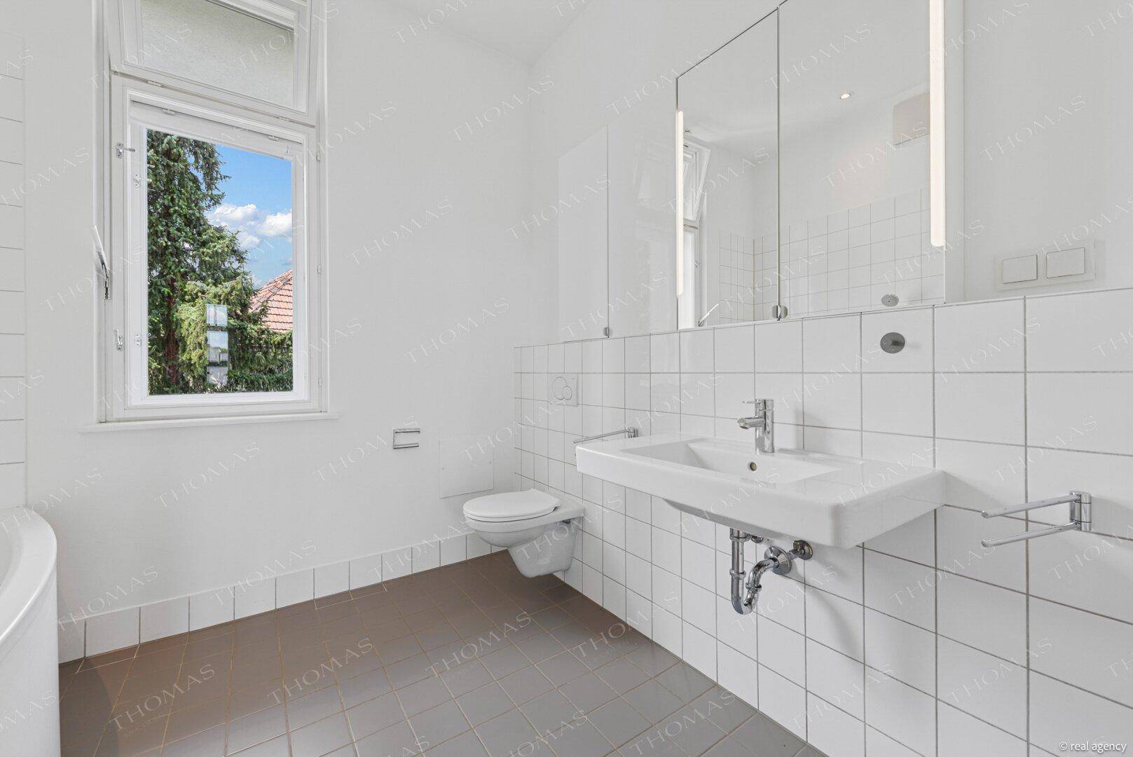 Helles Badezimmer mit weißen Fliesen, modernem Waschbecken, Spiegelschrank und Fenster.