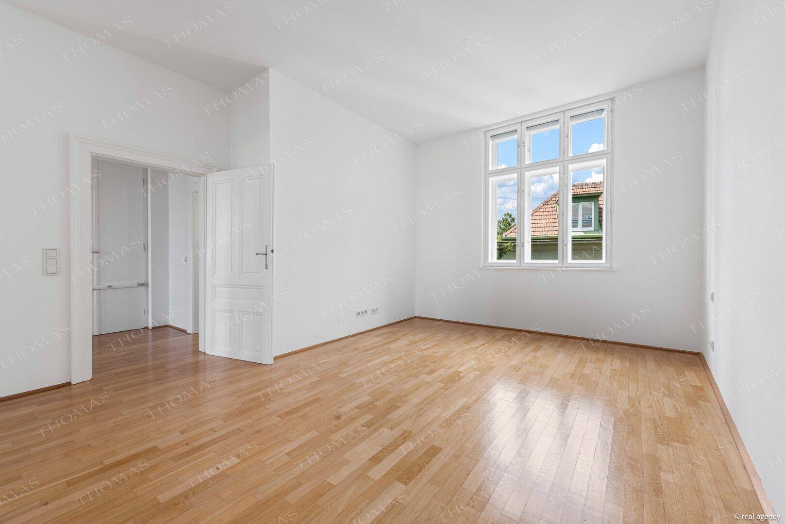 Ruhiges Zimmer mit Parkettboden und großem Fenster, das einen Blick ins Grüne bietet.