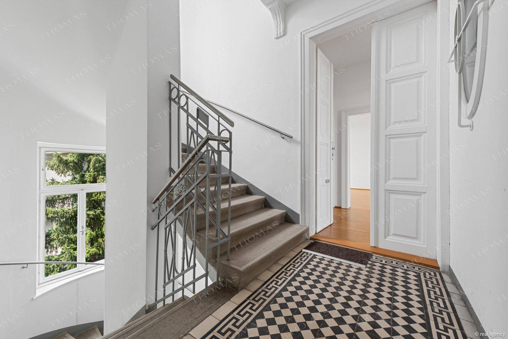 Heller Treppenaufgang in einem Altbau mit charakteristischen Fliesen und hohen Decken.