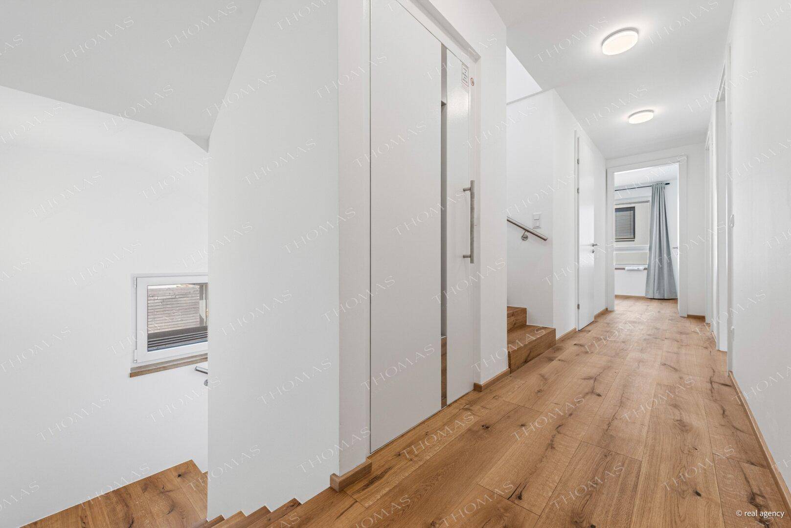 Langer, heller Flur mit Holzboden und Zugang zu verschiedenen Zimmern und einer Treppe.