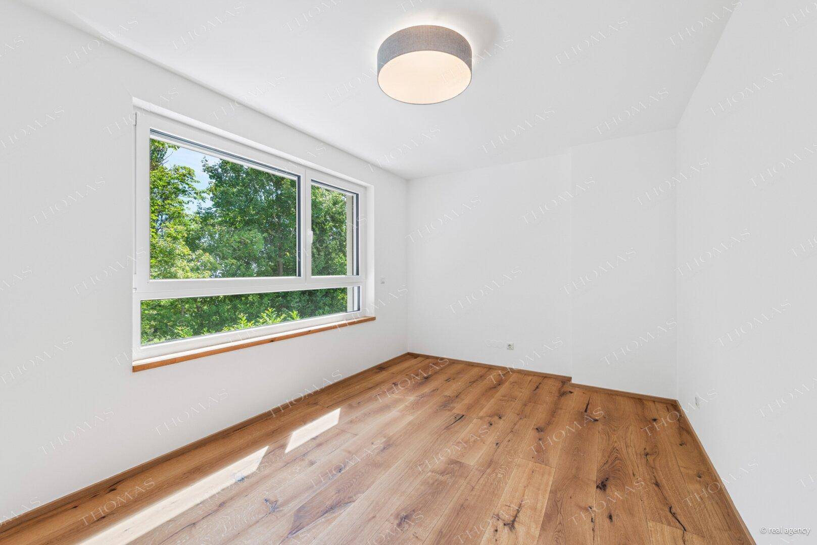 Helles Schlafzimmer mit Holzboden und großem Fenster mit Blick ins Grüne.