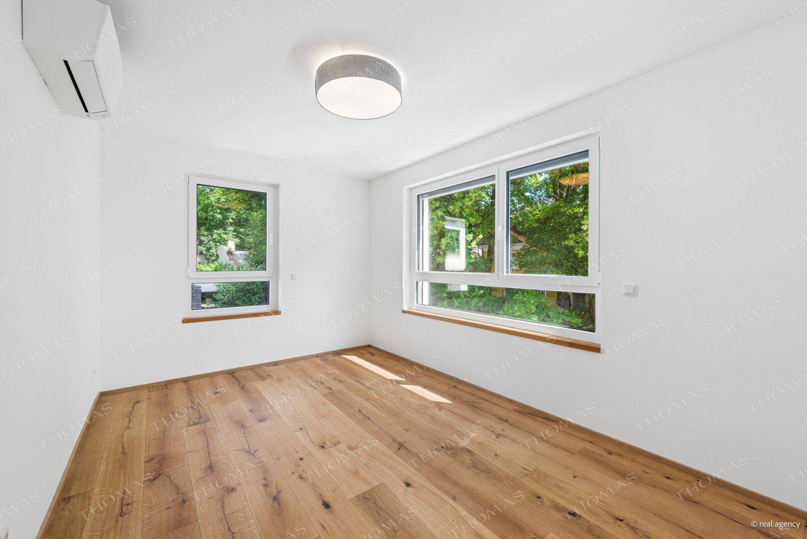 Geräumiges Schlafzimmer mit Holzboden, zwei Fenstern und Klimaanlage.