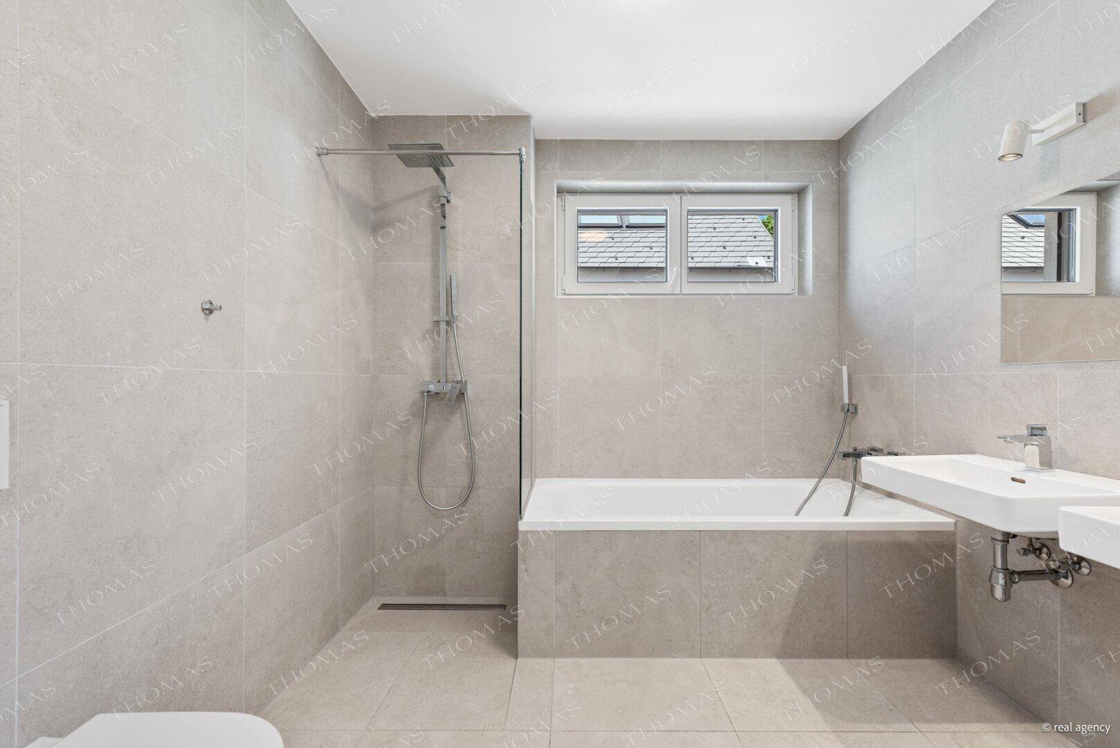 Modernes Badezimmer mit grauen Fliesen, Badewanne, Dusche und Fenster.