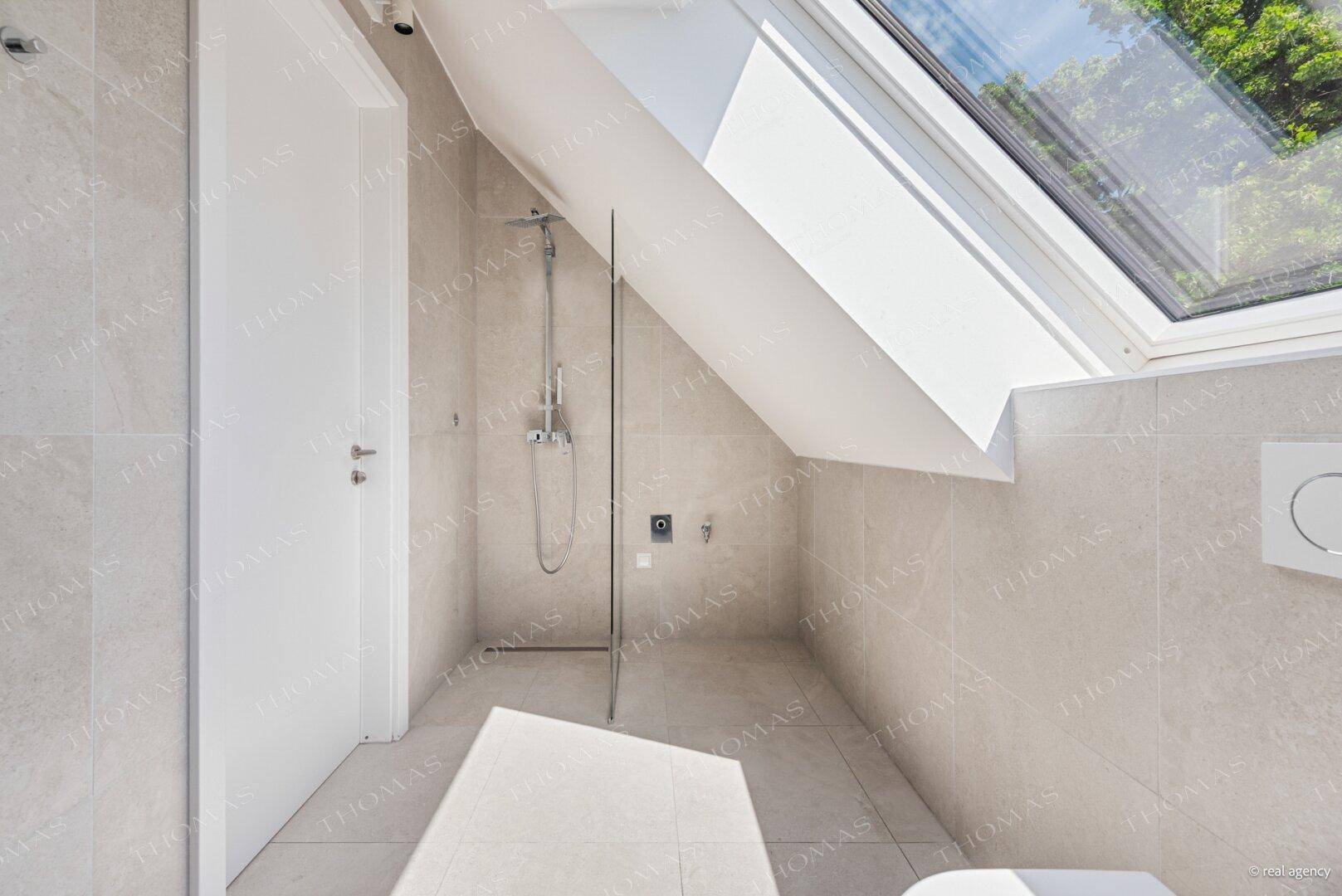 Helles WC mit Dusche, grauen Fliesen, wandhängender Toilette und großem Dachfenster.