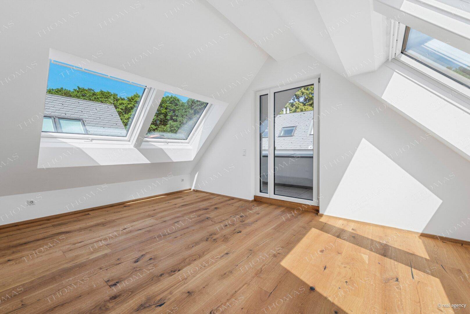 Geräumiges Dachzimmer mit Holzboden, vielen Dachfenstern und Zugang zu einem französischen Balkon.