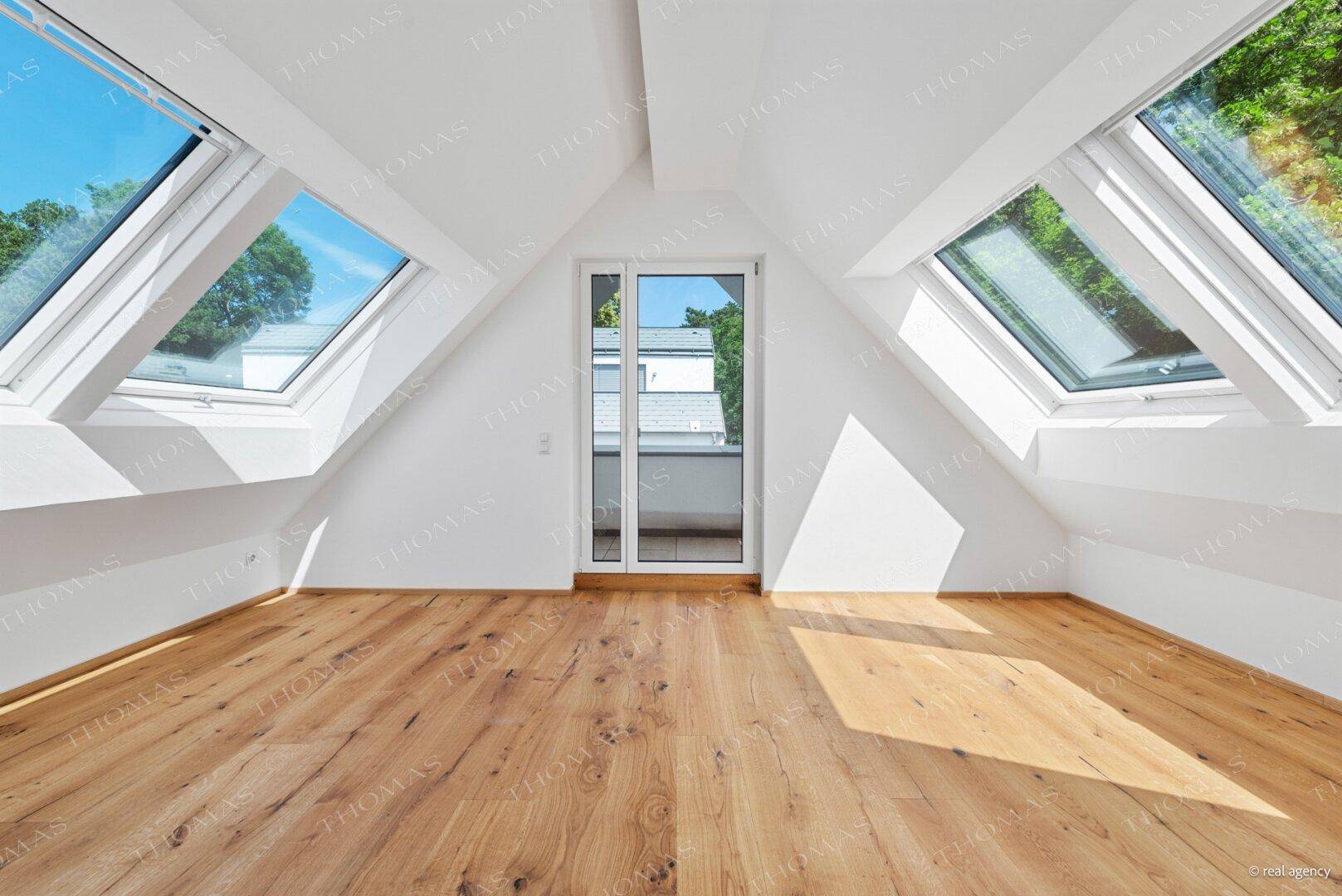 Helles Zimmer im Dachgeschoss mit Holzboden, Dachfenstern und französischem Balkon.