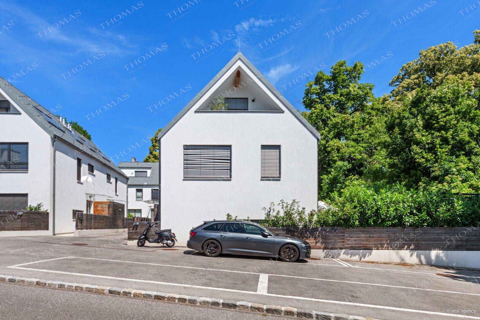 Moderne weiße Hausfassade mit Satteldach, großen Fenstern und einem geparkten Auto davor.