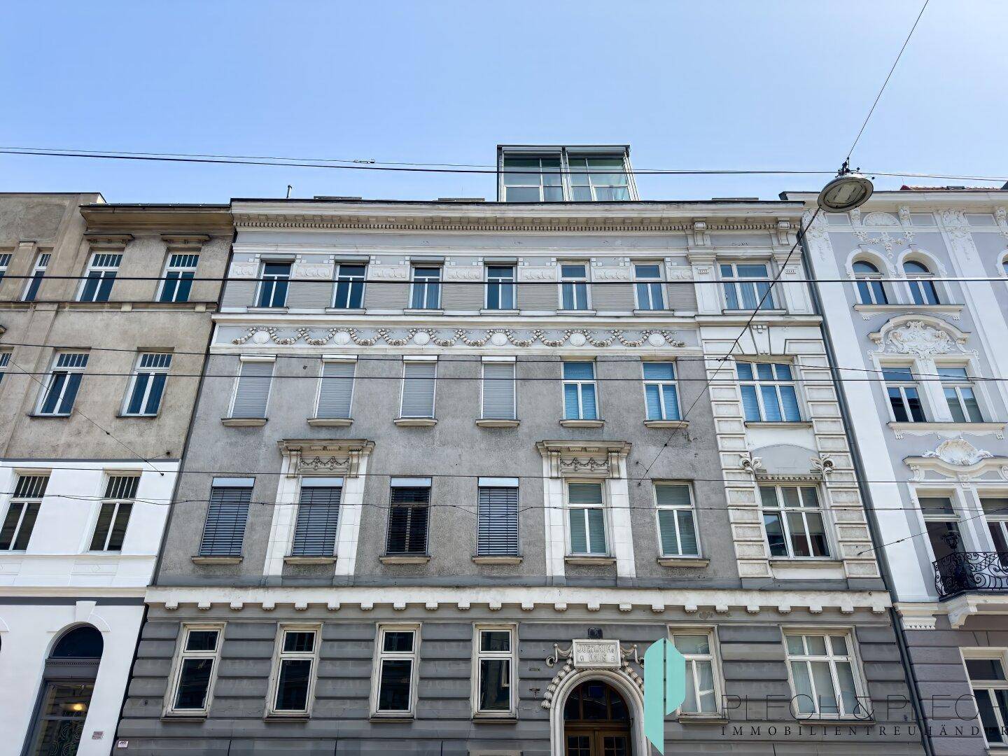 Fassade eines historischen Gebäudes mit vielen Fenstern und einem modernen Dachaufbau.