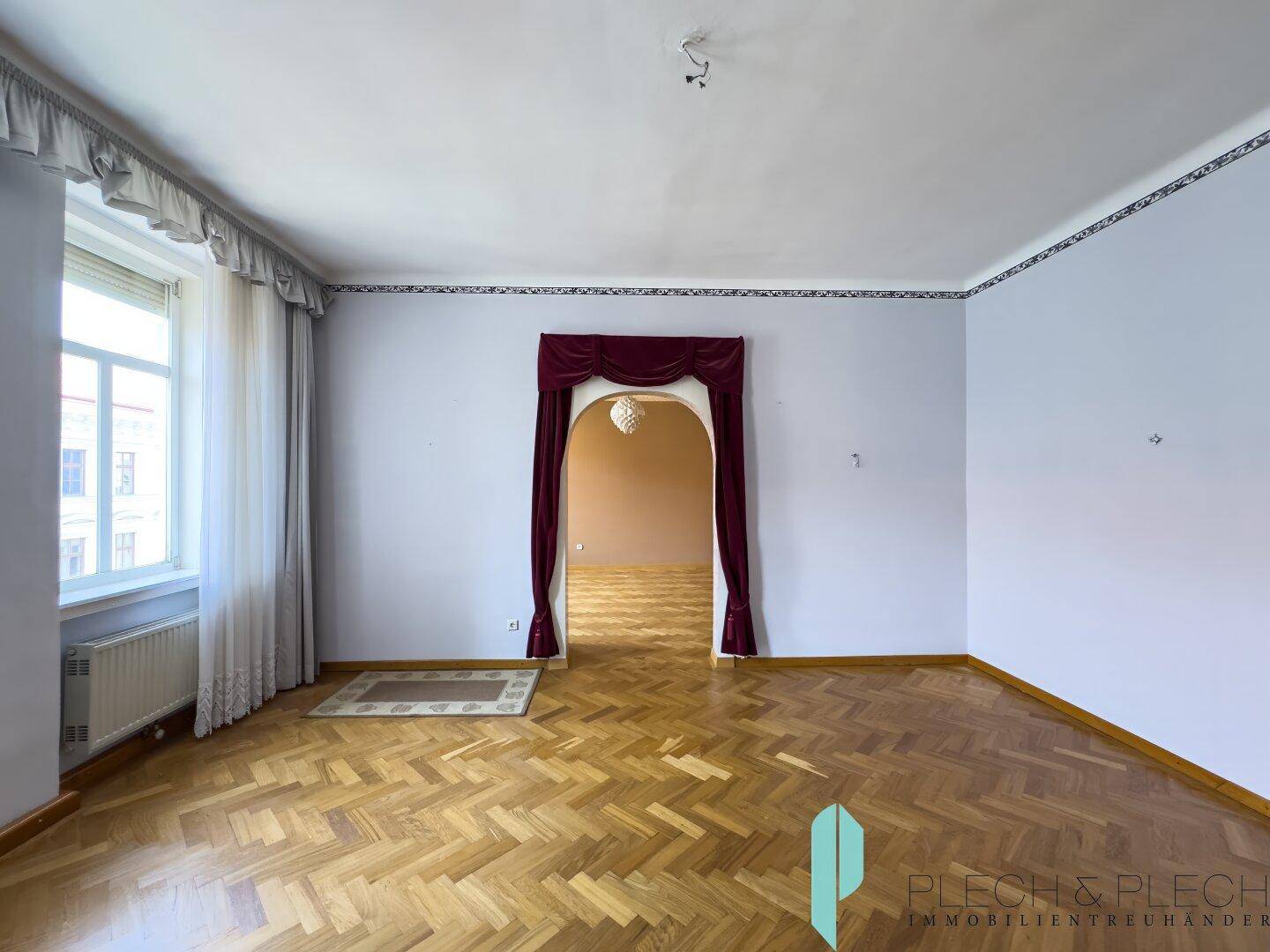 Helles Wohnzimmer mit klassischem Fischgrätparkett und einem eleganten Türbogen.