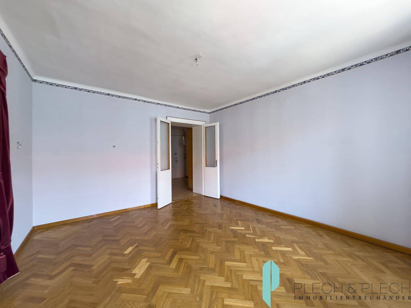 Großes Zimmer mit Fischgrätparkett und Doppeltüren, ideal für flexible Wohnkonzepte.
