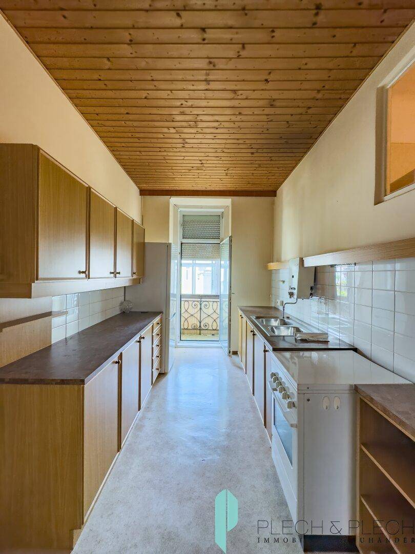 Schmale Küche mit Holzdecke, Einbauschränken und Zugang zu einem kleinen Balkon.