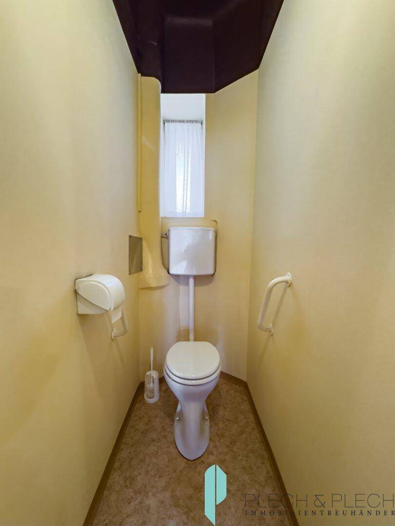 Separate Toilette mit Fenster und Haltegriff, in schlichtem Design.
