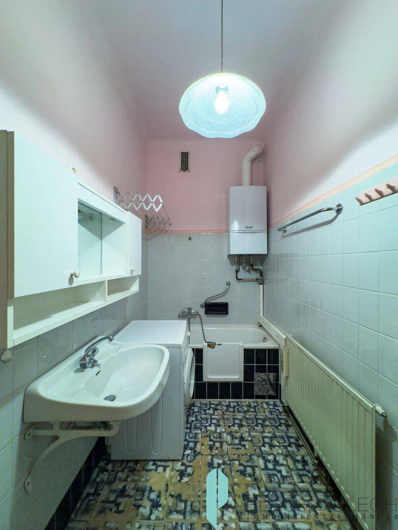 Badezimmer mit Badewanne, Waschbecken und Waschmaschine, in renovierungsbedürftigem Zustand.
