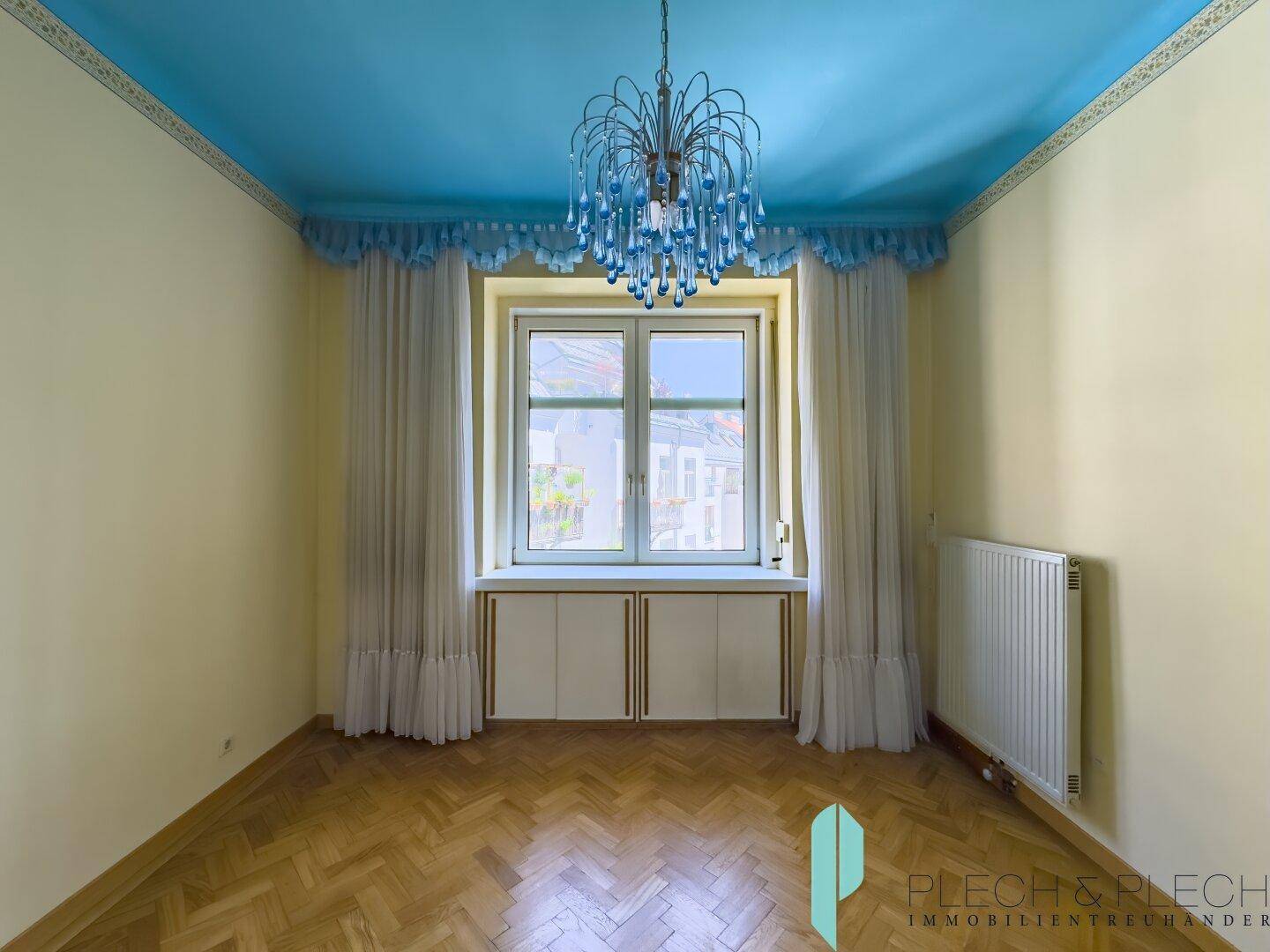 Zimmer mit auffälliger blauer Decke, Fischgrätparkett und einem dekorativen Kronleuchter.