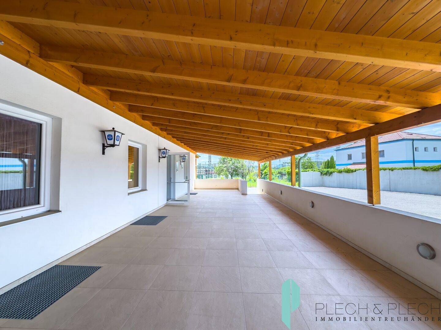 Überdachte Terrasse mit Fliesenboden und sichtbarer Holzdeckenkonstruktion, ideal für Entspannung.