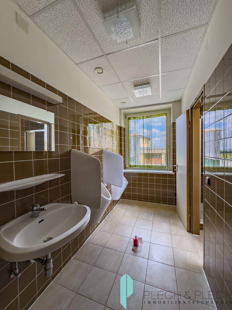 Herren-WC mit Fliesenboden, Urinalen und Waschbecken, ausgestattet mit Fenster.