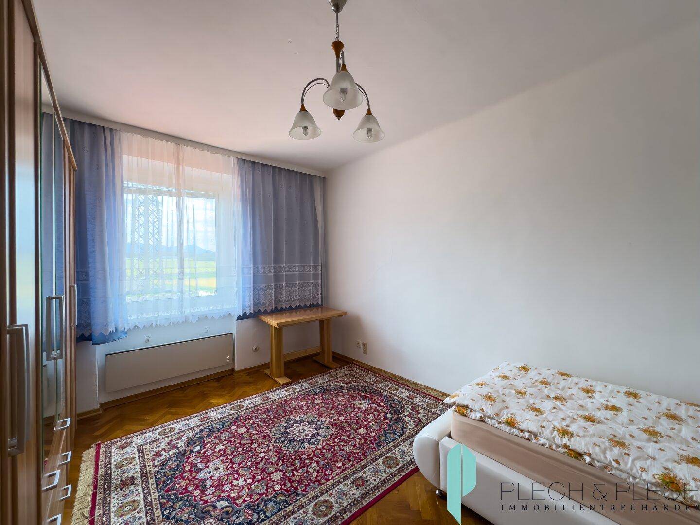 Gemütliches Schlafzimmer mit Einzelbett, Kleiderschrank und Fenster mit blauen Vorhängen und Holzboden.