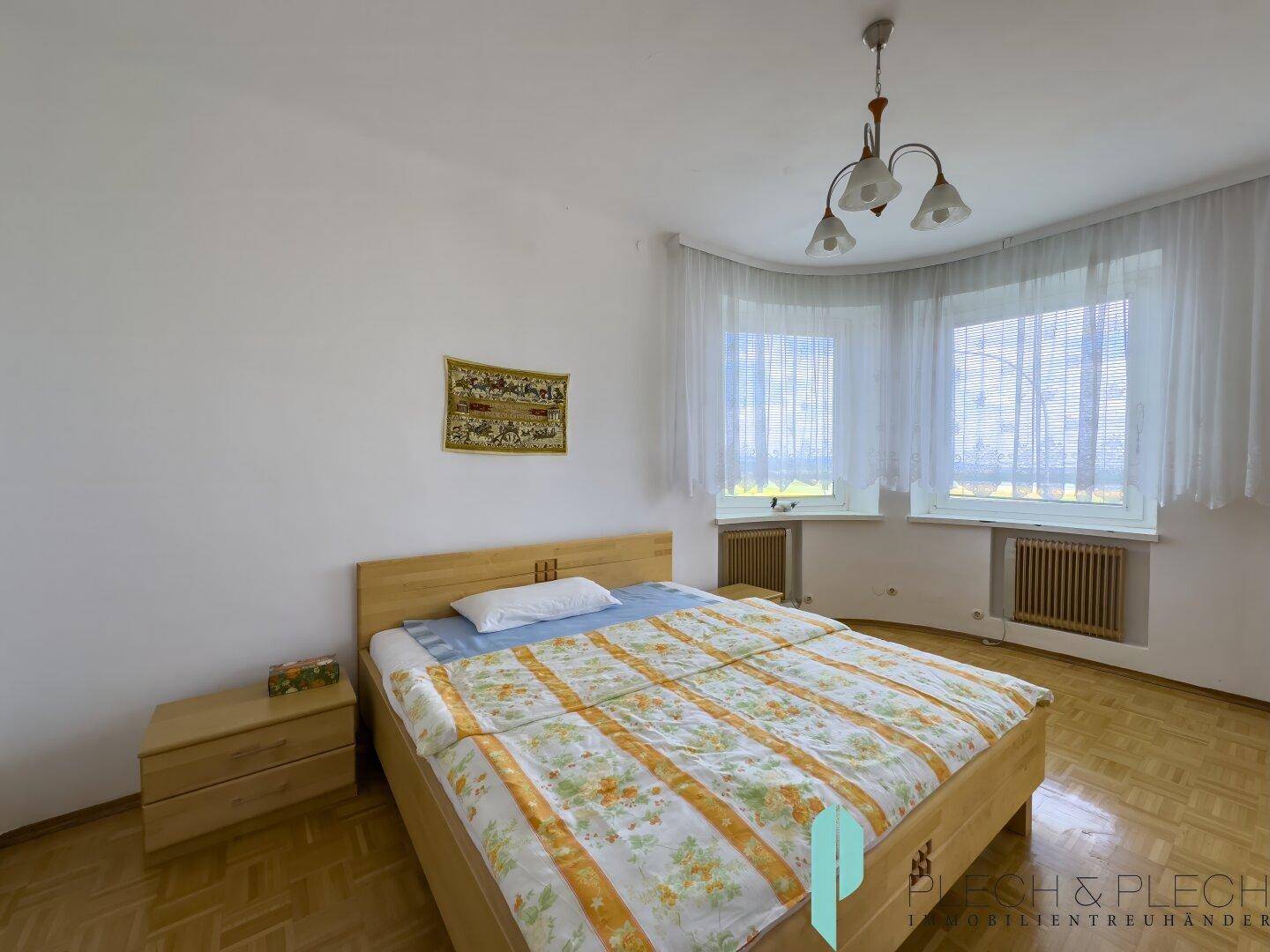 Geräumiges Schlafzimmer mit Doppelbett, Parkettboden und großen Fenstern für viel Licht.